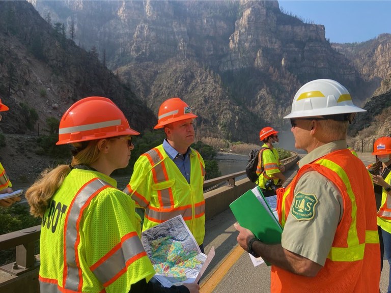Governor Polis, CDOT Director Lew, State Officials and members of the media observe the damage and repairs