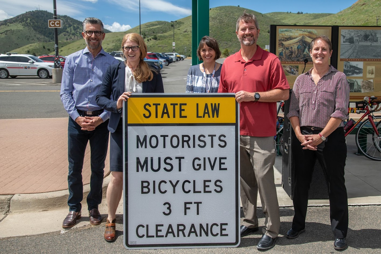 group of people with "Give bicyclists 3 ft. clearance" sign