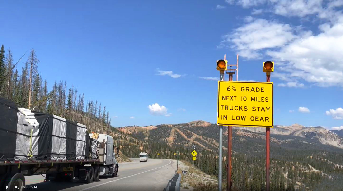 Trucker driving along a roadway on a mountain pass with 6% grade for next 10 miles Trucks Stay in Low Gear sign detail image