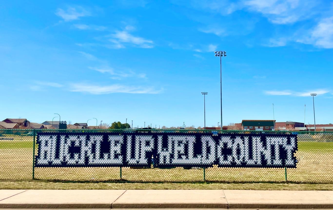 Bulldogs Buckle for Safety with Buckle Up Weld County message installed with fence cups in chain-link fence at University High School in Greeley..png detail image