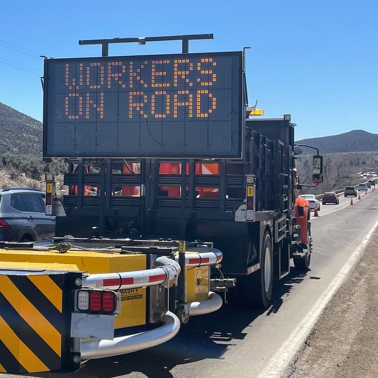 Image of a sign in a construction zone. Sign has text text reading, "Workers on road."