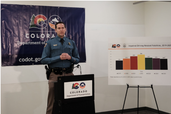  Colorado State Patrol Chief Matthew Packard speaking at a press conference. He is in front of a blue Colorado Department of Transportation banner and next to a graph showing impaired driving-related fatalities from 2019-2025.”