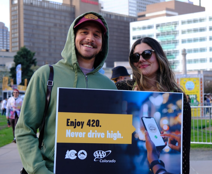 Man and woman standing in Denver’s Civic Center Park holding a sign that reads “Enjoy 420. Never drive high.”