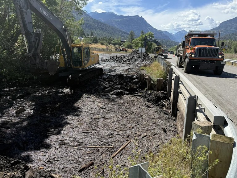 CDOT Crew operating an excavator with specialized attachment to clean flood debris on the side of the road