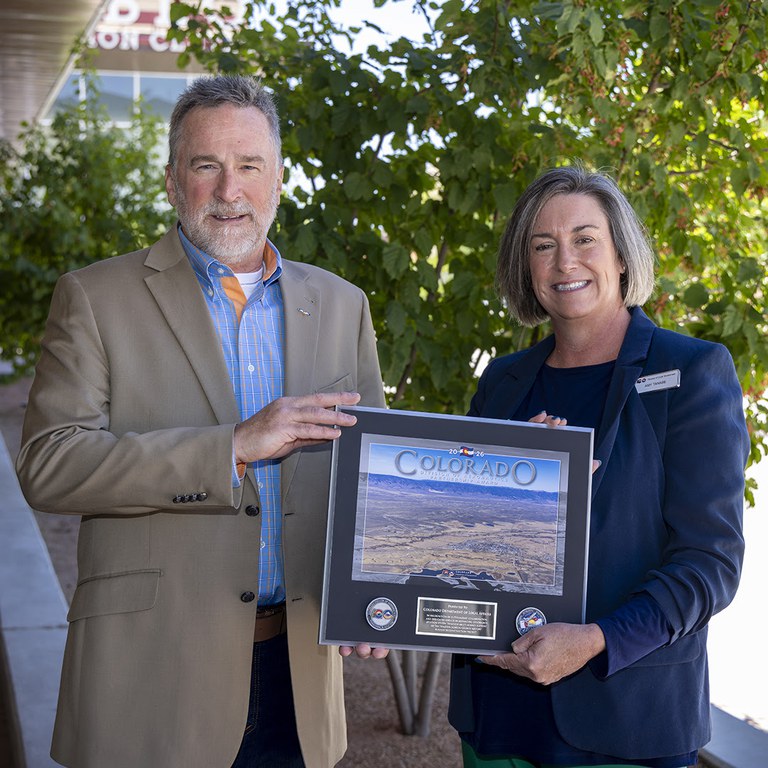 Division of Aeronautics Director David Ulane (left) presents the Division's Partnership Award to Amy Tanabe, Southeast Regional Manager for the Colorado Department of Local Affairs (DOLA) (right).