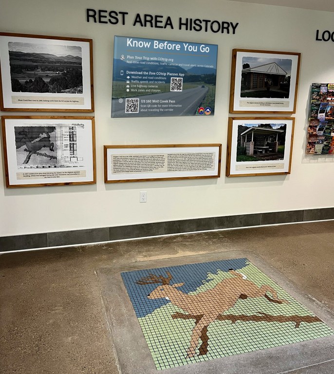 The preserved mosaic tile mural depicting a deer jumping over a barrier is inlaid on the floor below the wall of historical photos and facts.