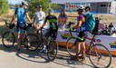 A photo showing a Colorado Department of Transportation (CDOT) Bike to Work Day station outdoors. Three staff members stand behind a table with a banner reading 'YOUR TRANSPORTATION PLAN'. A 'BIKE TO WORK DAY STATION' banner is in the background. Three cyclists in athletic wear and helmets with road bikes have stopped to talk to the staff. thumbnail image