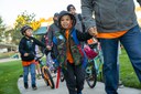 A smiling young boy wearing a hooded vest holding an adult's hand as they walk along a sidewalk on Walk to School Day, accompanied by other students and parents riding bicycles. Photo courtesy of Canyon Creek School District. thumbnail image