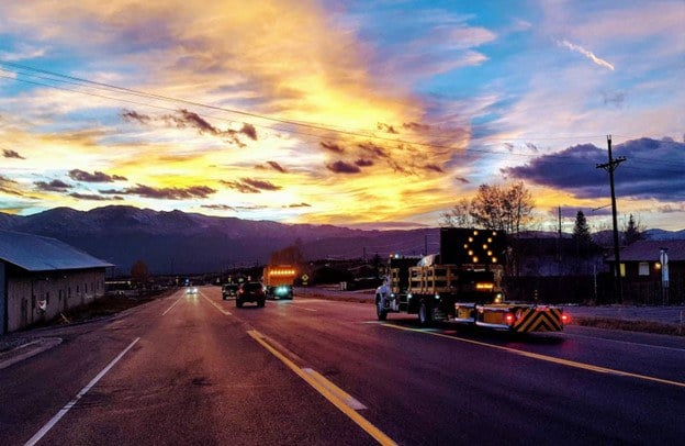  A group of CDOT trucks on a road at sunset.