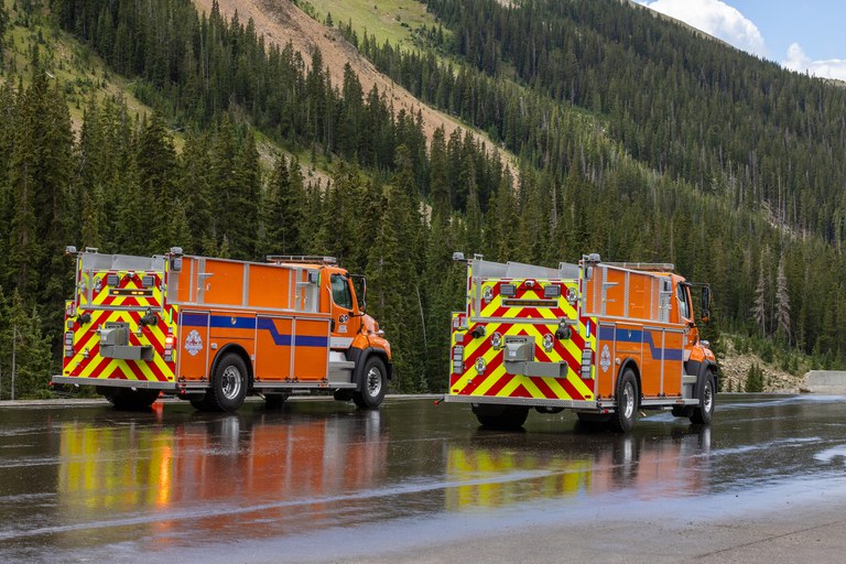 Two orange and one yellow fire truck on a mountain road.