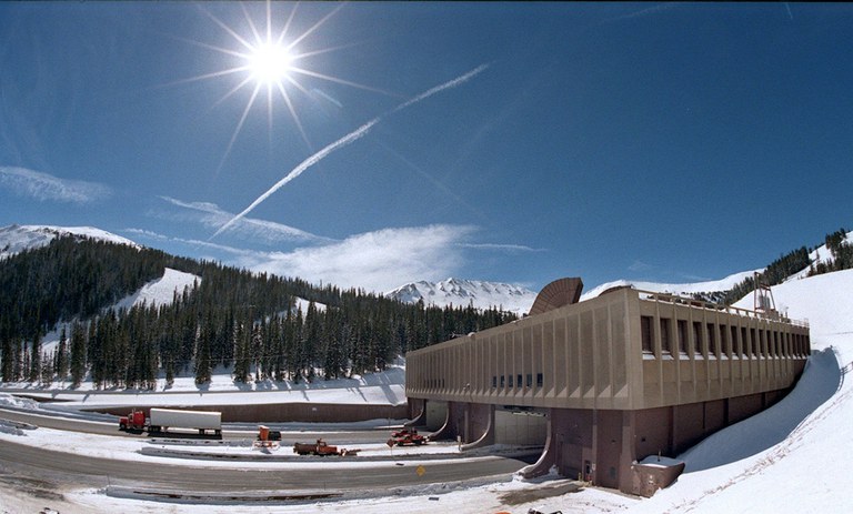 EJMT Sunny Sky Scenic Profile The Eisenhower-Johnson Memorial Tunnel and I-70 roadway embedded in a mountain surrounded by snow and pine trees.