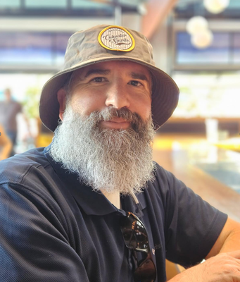 Portrait of Ken Howlett wearing a hat sitting at a table.