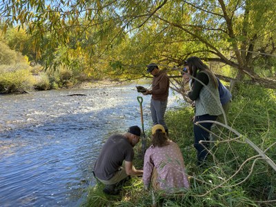 CDOT employees next to a river looking at books and soil with autumn foliage trees in the background.