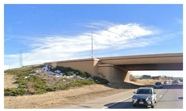 Photo of a bridge going over the highway that has several camera poles. 