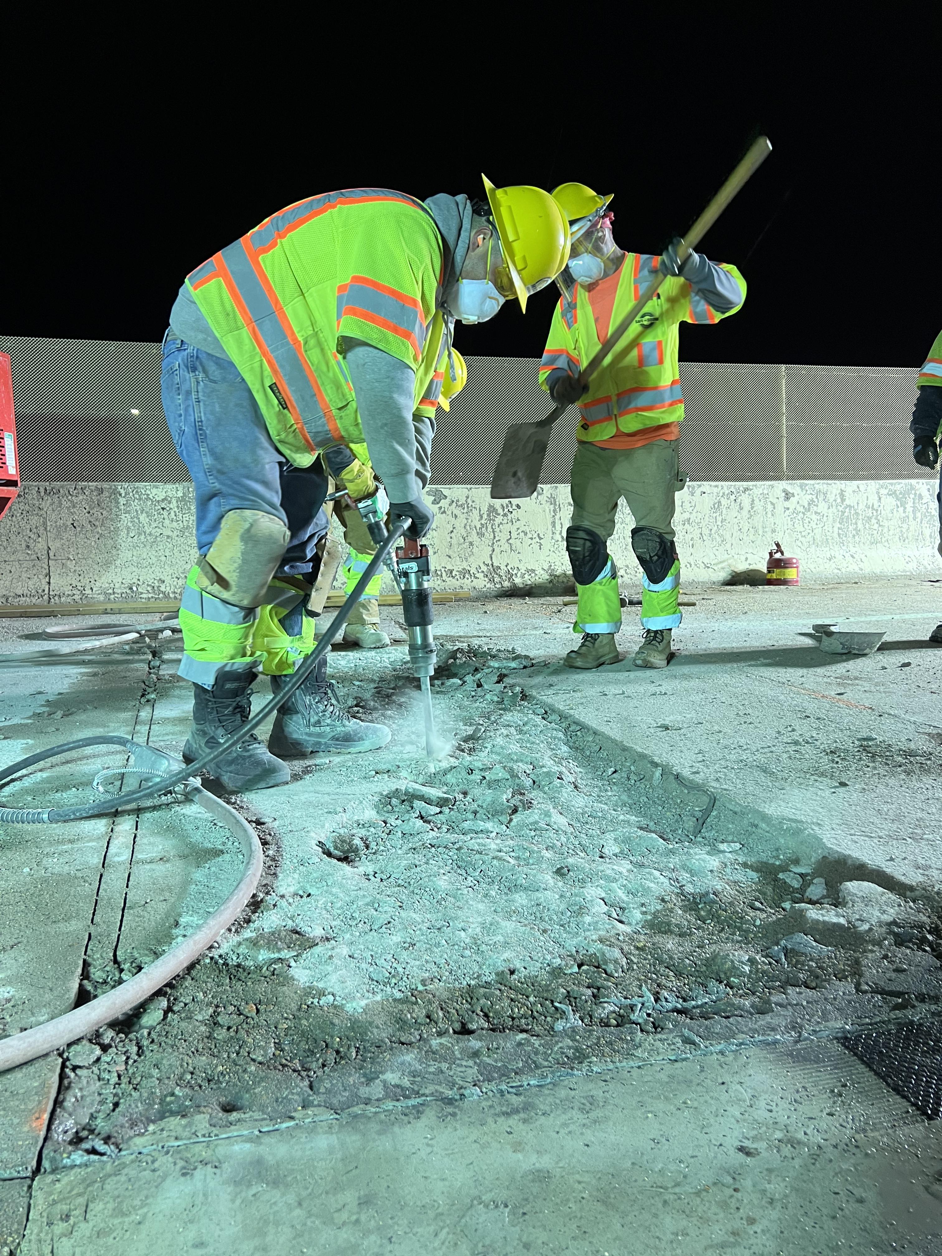 Two workers jack-hammering roadway on I-25 detail image