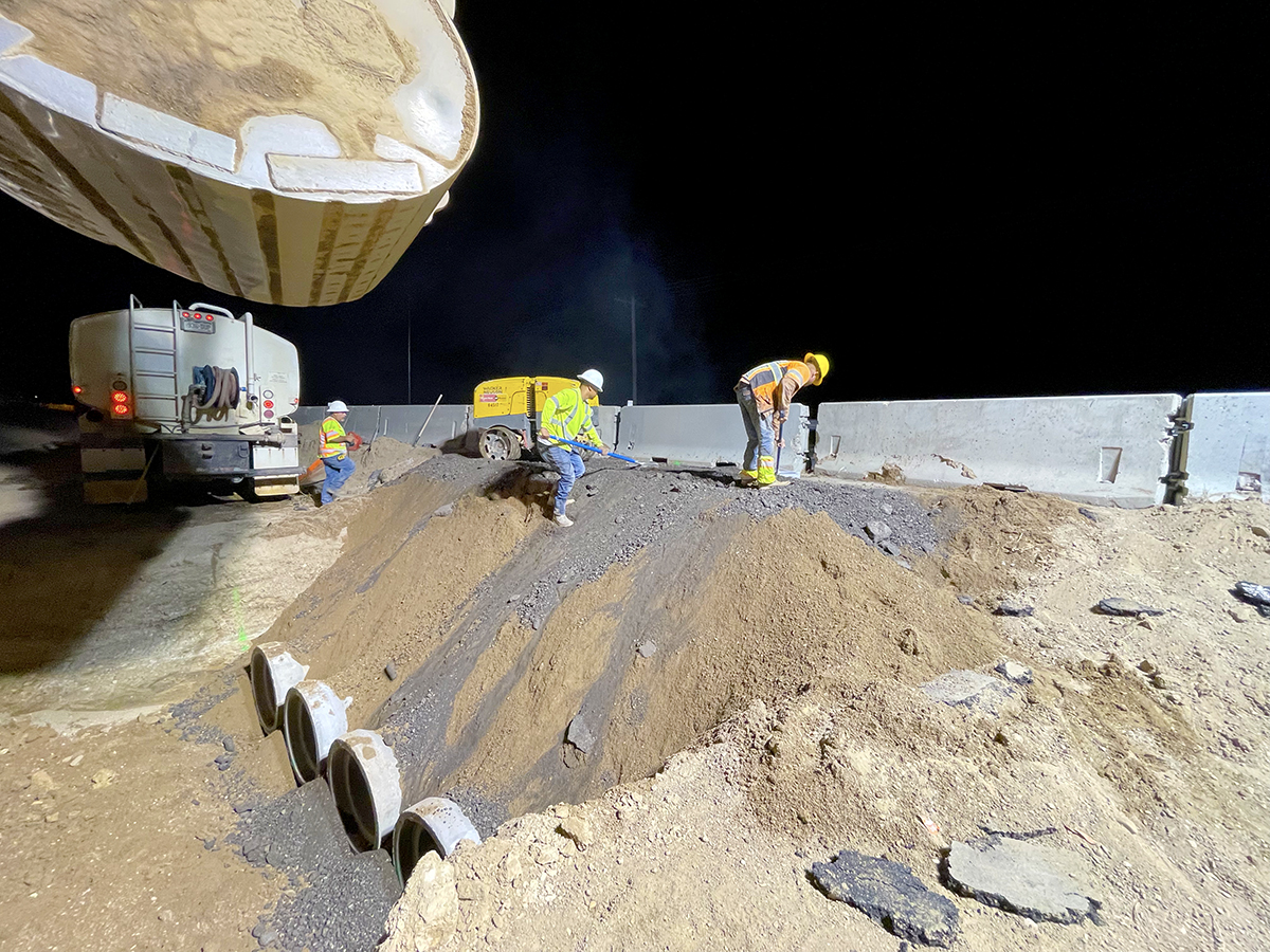 Workers look down to ground on top of large pile of dirt (at night) detail image