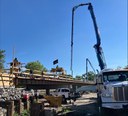 Concrete pump booms extend over the new CO 86 bridge in Kiowa as crews work on the deck, viewed from below. thumbnail image