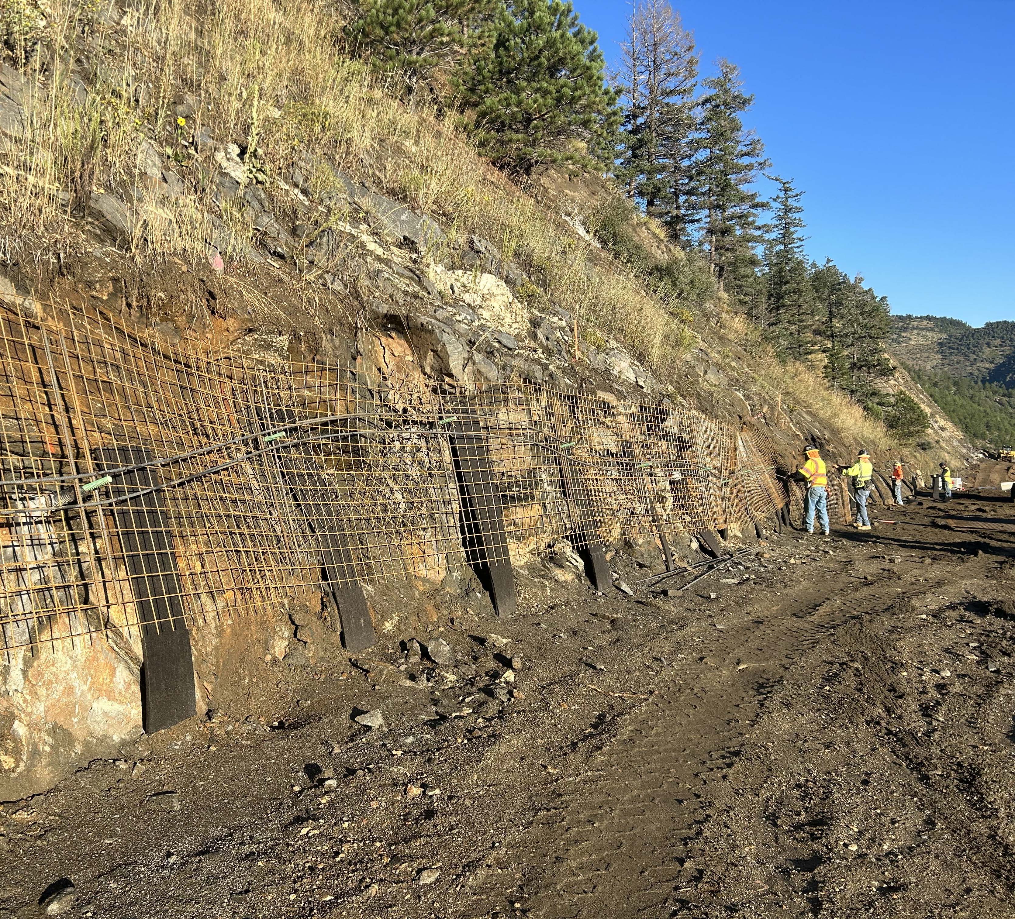 Crews working on soil nails | Alt text: People installing construction equipment on a hill wall. detail image