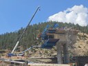 A concrete bridge pier and blue steel segment traveler under construction in a mountain pass, next to a large mobile crane. thumbnail image