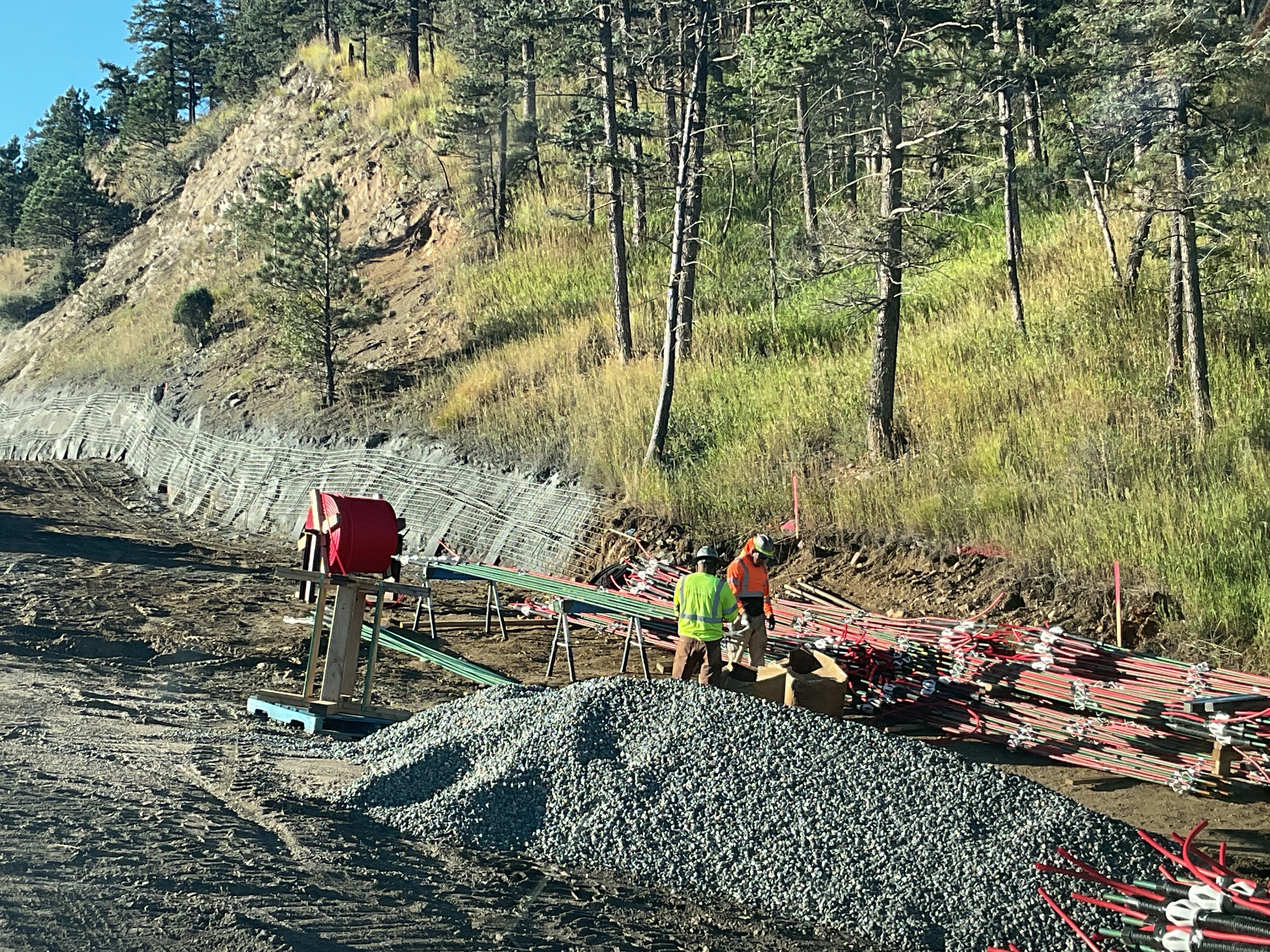 Crew members working on soil nails next to rebar and gravel pile detail image