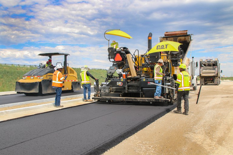 Construction workers conducting asphalt work on a dirt road. 