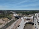 Aerial view of highway interchange construction showing new bridge spans over Union Pacific Railroad tracks and Fountain Creek, surrounded by dirt work, new roadway paving and active traffic lanes. thumbnail image