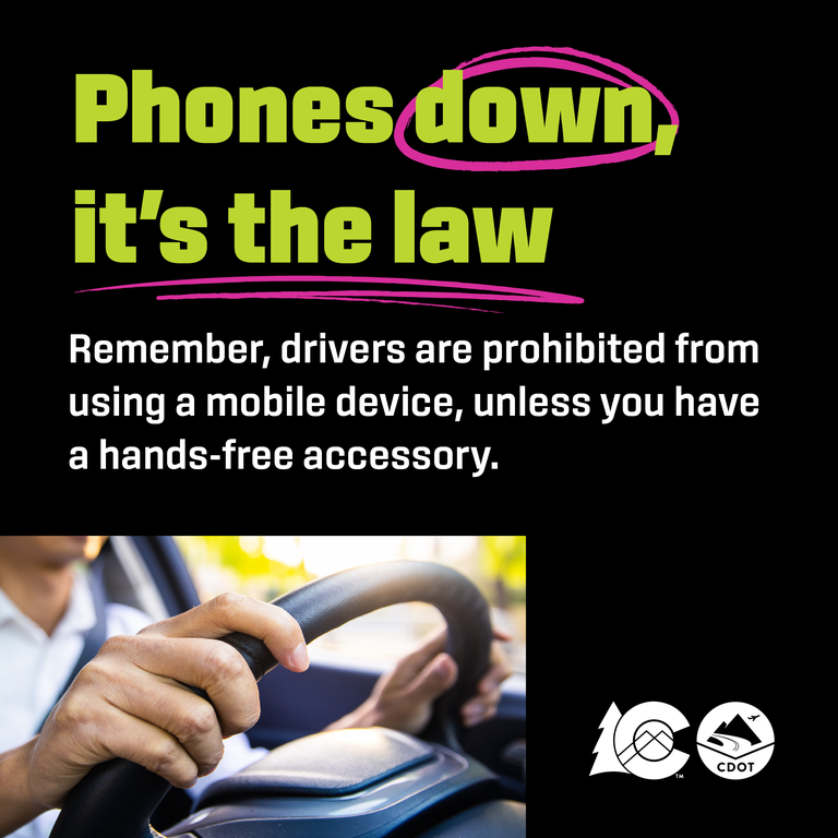 Person driving with both hands on the wheel. Text overlay reads "Phones down, it's the law"