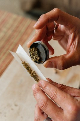 Hands holding a grinder and paper filled with cannabis