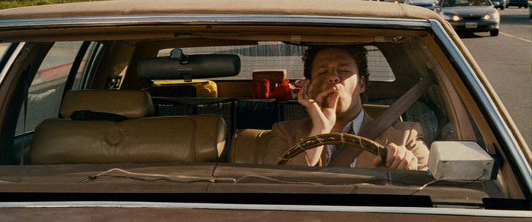 A driver holding a joint to his mouth while driving with one hand on the wheel. 