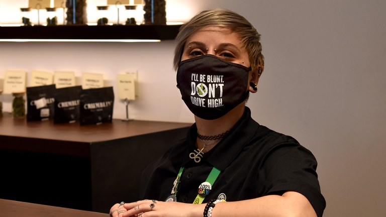 Budtender at dispensary wearing mask that reads "I'll be blunt, don't drive high"