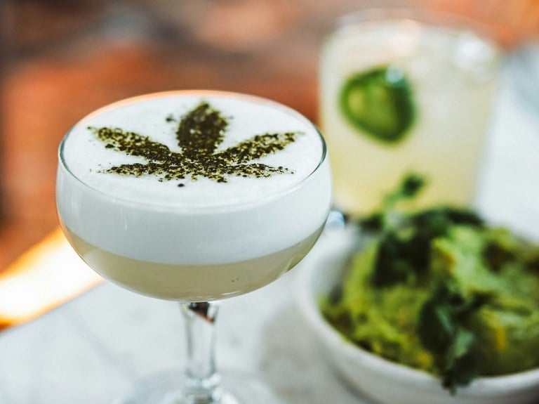 Alcoholic drink in a cocktail glass with cannabis leaf decor on top.
