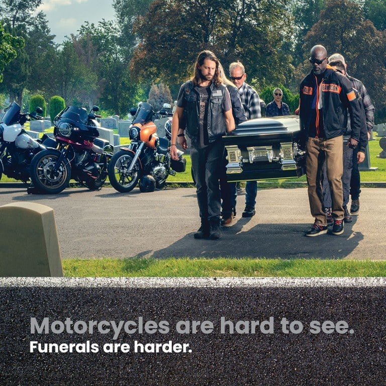 Image of a group of motorcyclists carrying a casket through a graveyard