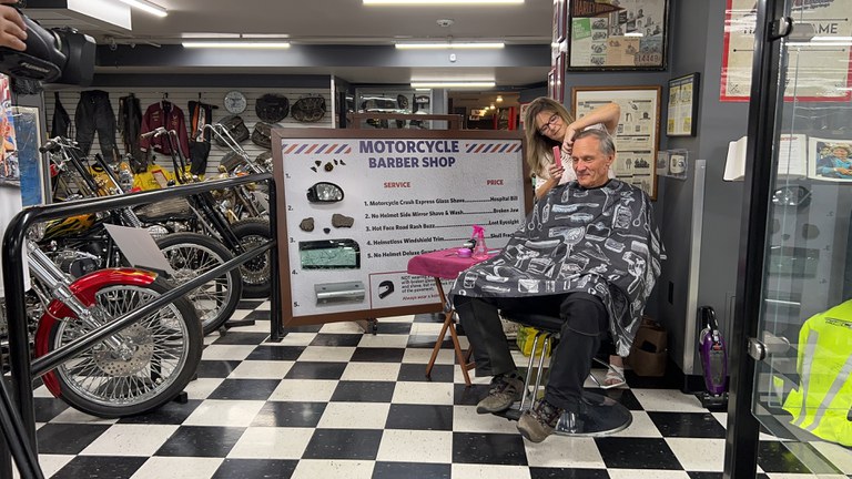 Motorcycle rider is receiving a haircut from a barber