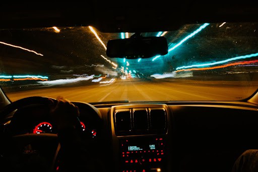 View from inside a car looking out into the street at night. The street and car lights are streaked and blurred, indicating that the car is speeding and the driver may be impaired. 