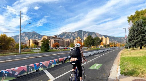 A person bikes on Baseline Road in Boulder's new protected bike lane with a tall curb painted by artist Talia Swartz Parsell 