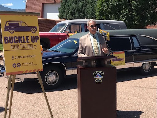 Glenn Davis, CDOT employee, speaking in front of hearses covered in Click it or Ticket messaging. A banner is next to him that says, "Buckle up, avoid this ride. Click it or Ticket. Colorado Department of Transportation."