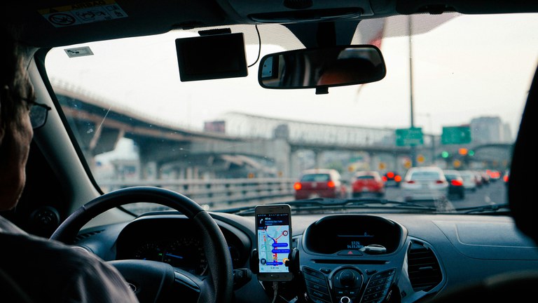 A man driving his car on a highway with his phone on the dashboard with a navigation map on it. 