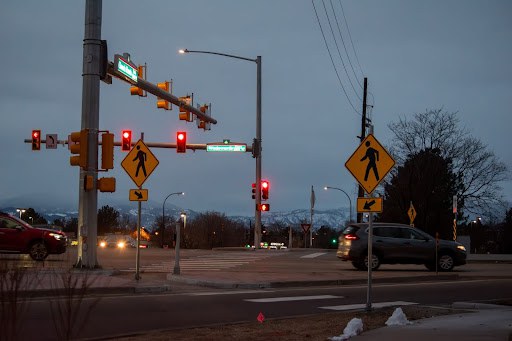 Cars drive past new pedestrian signage on a dark February evening at the intersection of Wadsworth Parkway and 100th Avenue. 