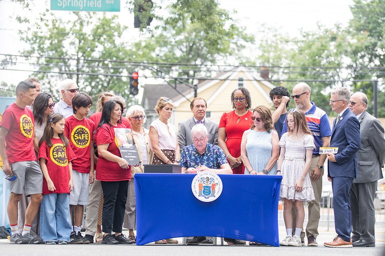 People standing around a table with blue tablecloth as New Jersey Gov. Phil Murphy signs new legislation. 