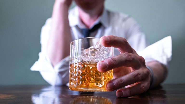 Man in white dress shirt holding a glass filled with brown liquor.