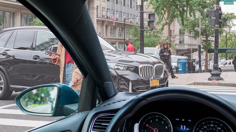 Vehicle entering a crowded intersection with pedestrians and black SUV. 