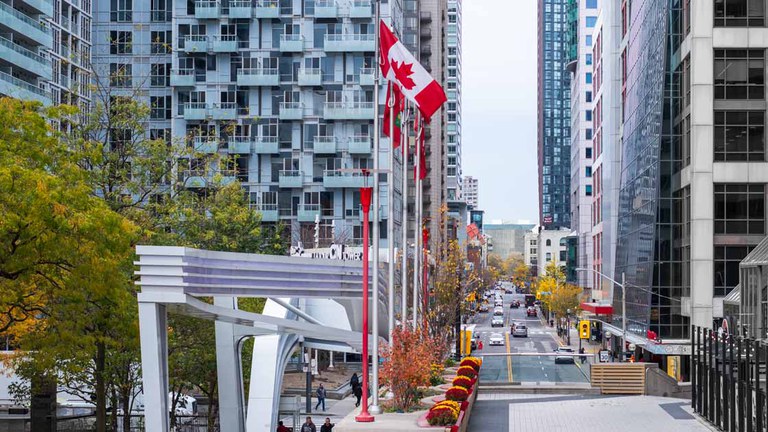 Strong road safety policies in Canada Urban street with cars, tall buildings and a flagpole with the Canadian flag.
