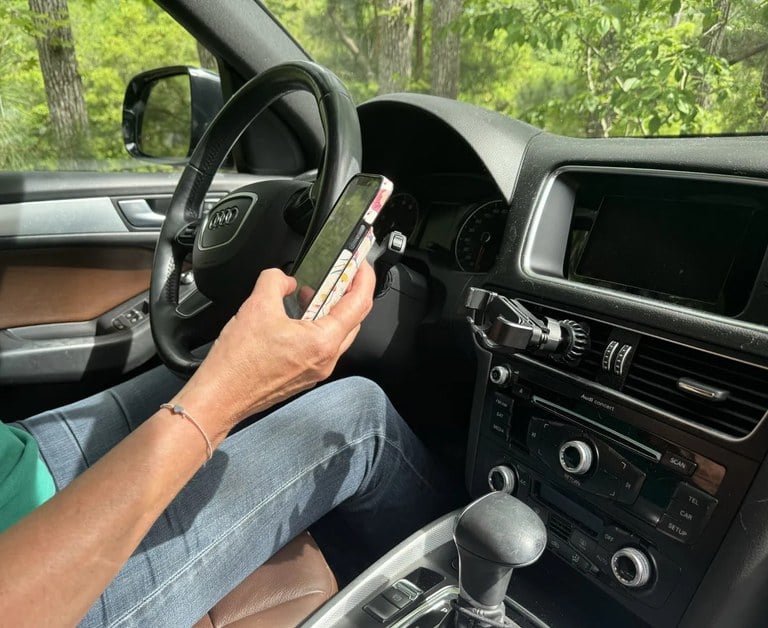 Person sitting in the driver’s seat of a vehicle and holding cellphone in right hand.