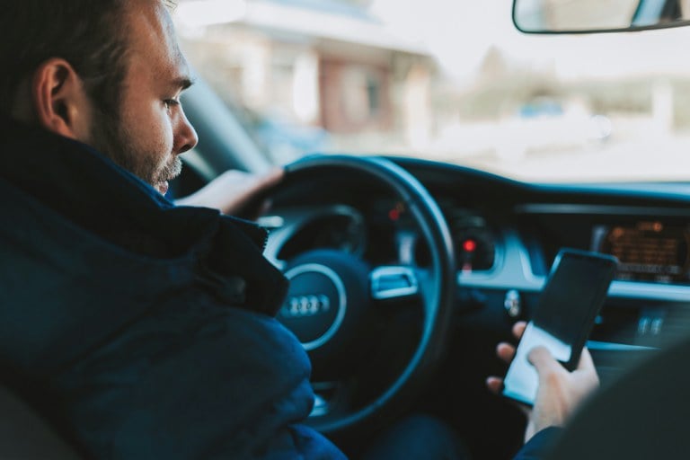 Man driving car and holding cellphone in his right hand.