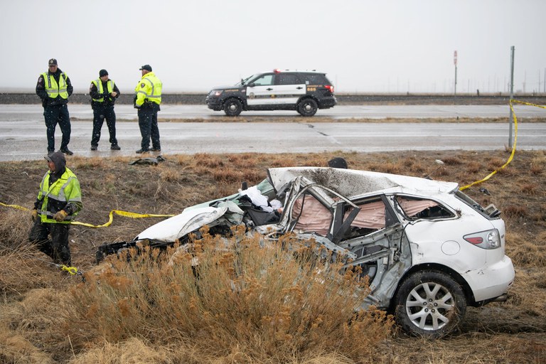 White SUV crashed in a grassy median with a police car and police officers on the road. 