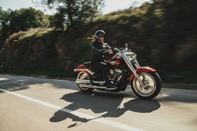 Person riding red motorcycle or rural highway with trees lining the road.