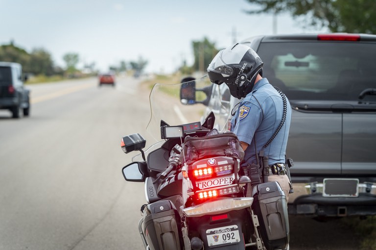 CSP Troop Ride Along 156 Colorado State Patrol motorcycle and trooper behind a grey SUV on the side of the road with vehicles passing on the left.