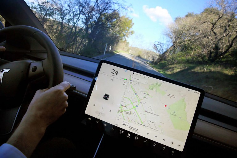 Watching YouTube and TikTok behind the wheel Interior of a Telsa with the driver’s hands on the steering wheel and a map displayed on the vehicle’s screen.