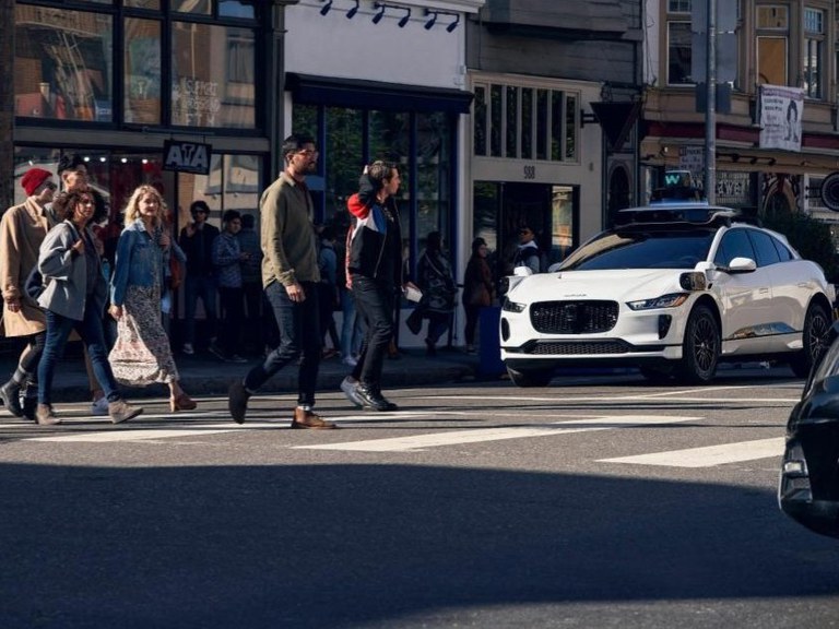  A Waymo driverless car waits as pedestrians cross the street.