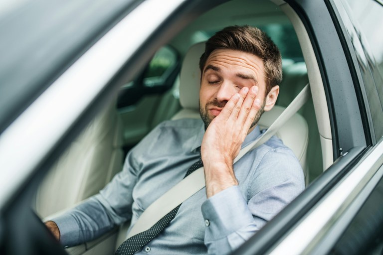 Man in the driver’s seat of a vehicle with his eyes closed and left hand on his face.